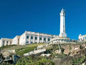 Historic Alcatraz Island cellhouse and white lighthouse towering over rocky cliffs on a clear day in San Francisco Bay